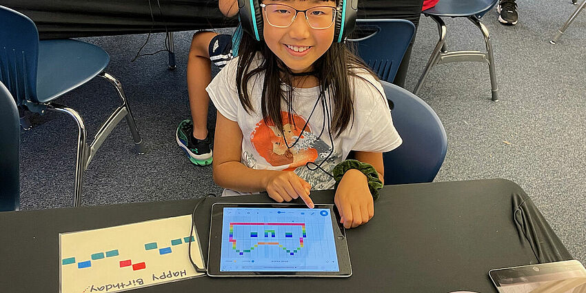 young girl wearing headphones and using a computer device to make music