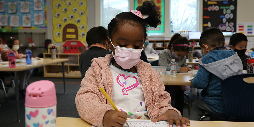 little girl in mask doing school work in class