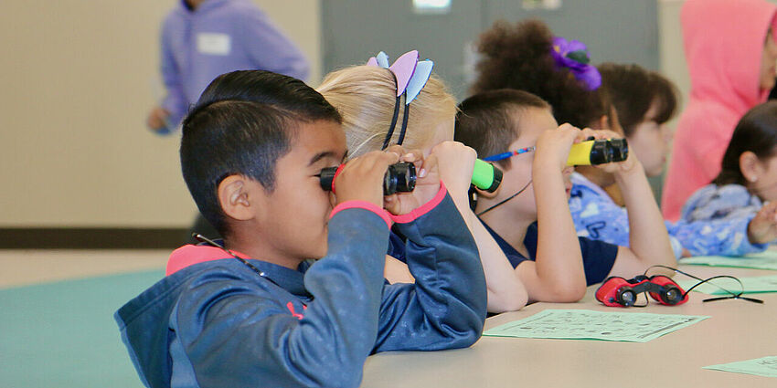 a row of kindergarten students looking through binoculars