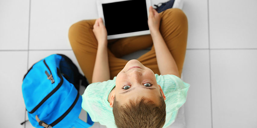 young boy holding tablet and looking up