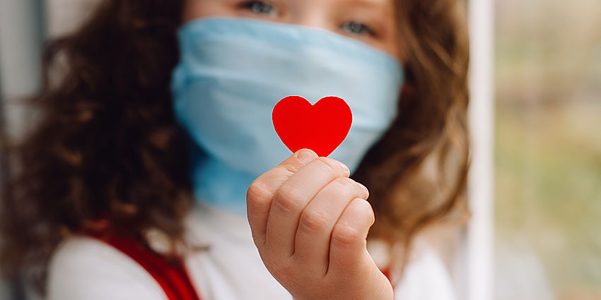 young girl wearing face mask holding a red heart sticker