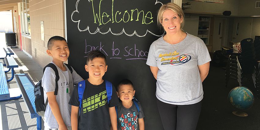 A teacher with 3 students in front of a welcome sign