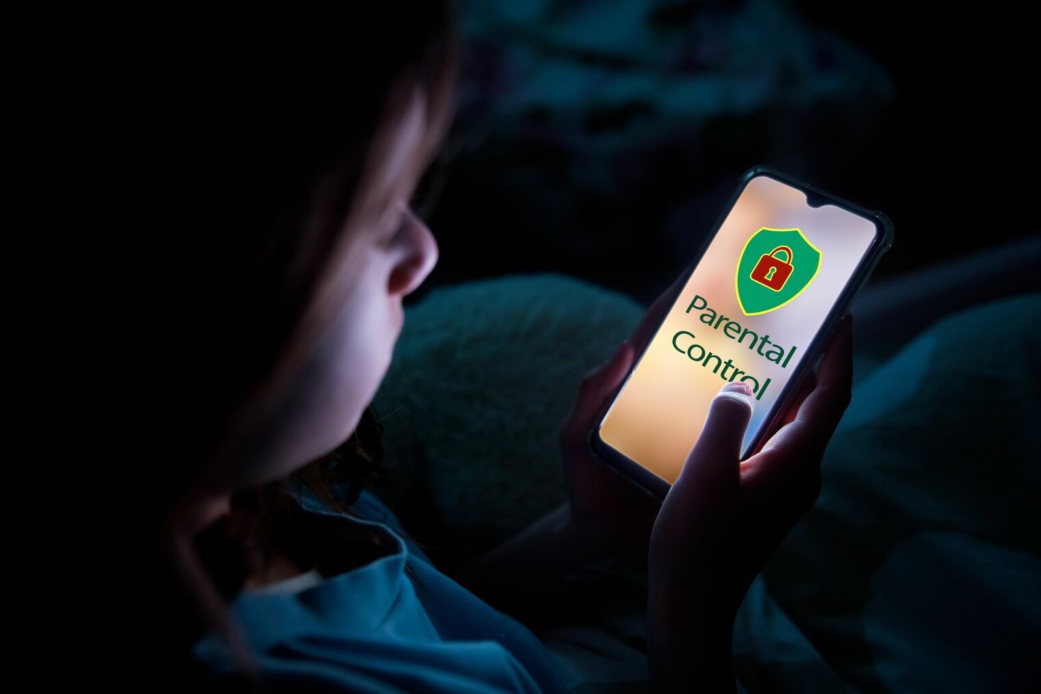 young child in a dark room looking at a lighted smartphone screen that says 