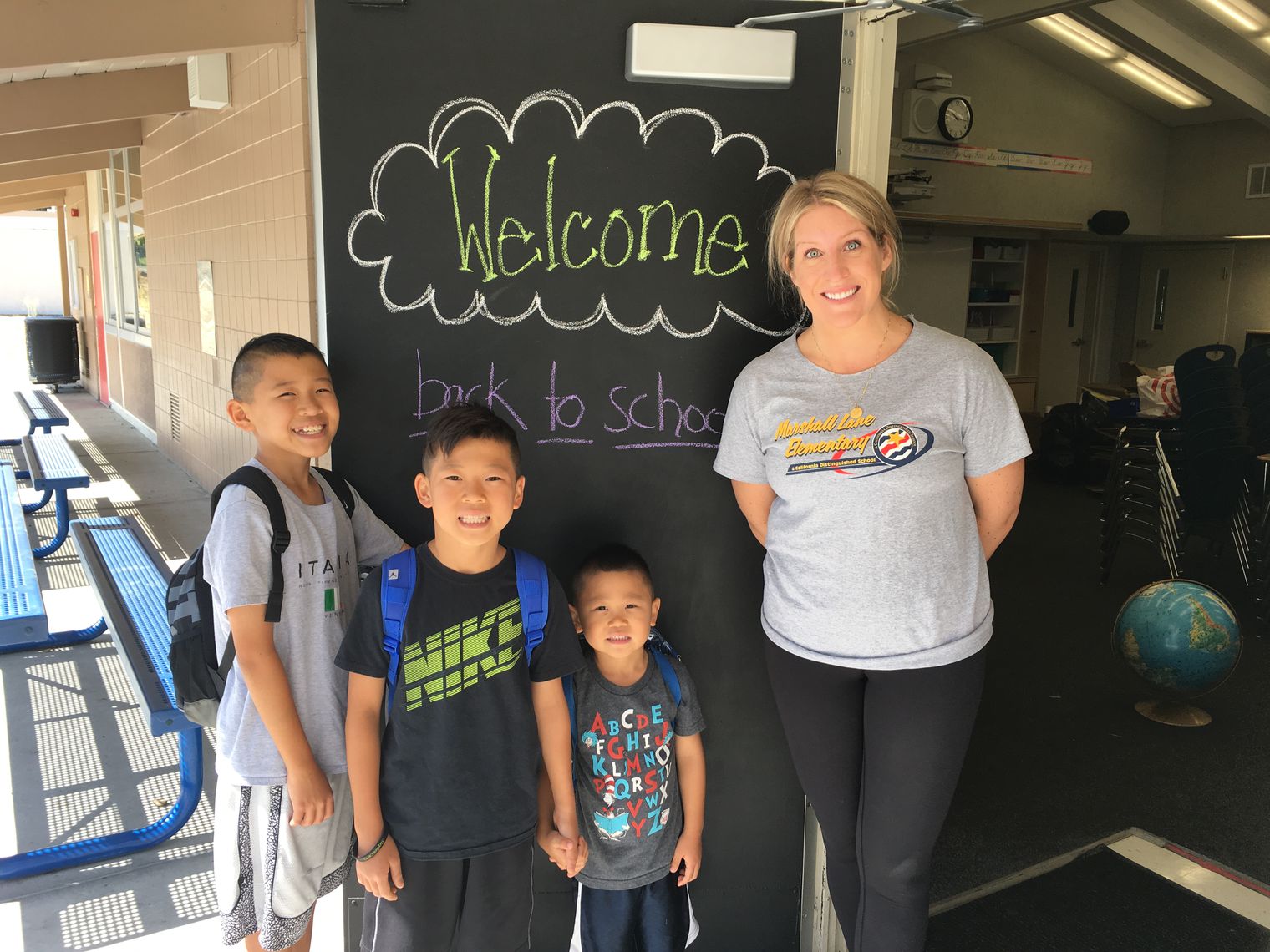 A teacher with 3 students in front of a welcome sign